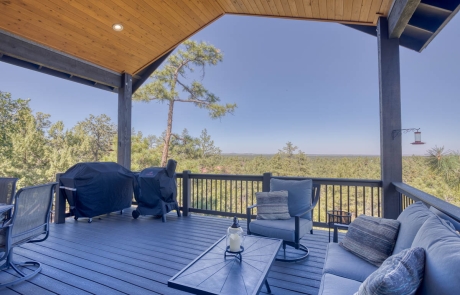 Spacious outdoor deck with wooden flooring, surrounded by lush trees and open sky. Tranquil setting in Show Low, Arizona.