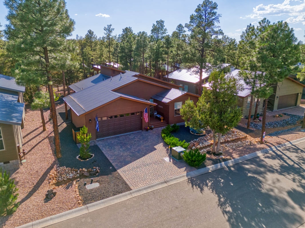 Home surrounded by pine trees, stone landscaping, paved driveway, for sale in Show Low, Arizona.